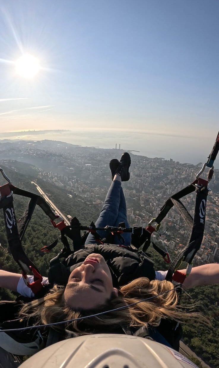 Heart-shaped hands framing the sunset over Jounieh Bay while paragliding
